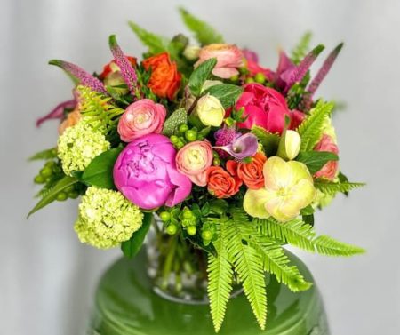 A delightful dense arrangement of coral and pink peonies, ranunculus, hellebores and other premium garden flowers.