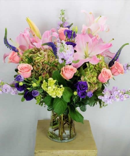 Opulent bouquet of purple, blush and green fresh cut flowers designed to impress in a tall clear glass vessel!