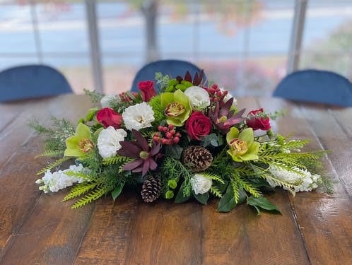 Classic long and low centerpice of winter greens accented with designers choice of best availalbe red, white and green flowers. 