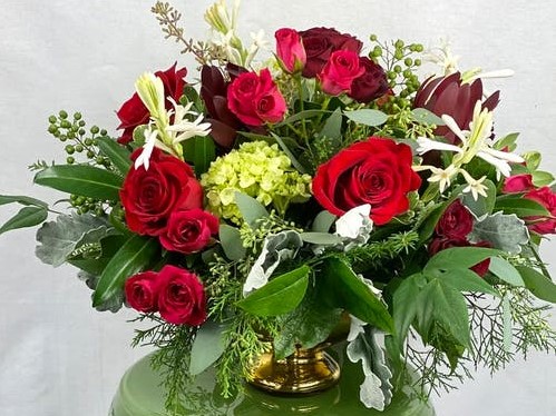 Gold footed bowl overflowing with bright red roses and other garden flowers in white and green. 