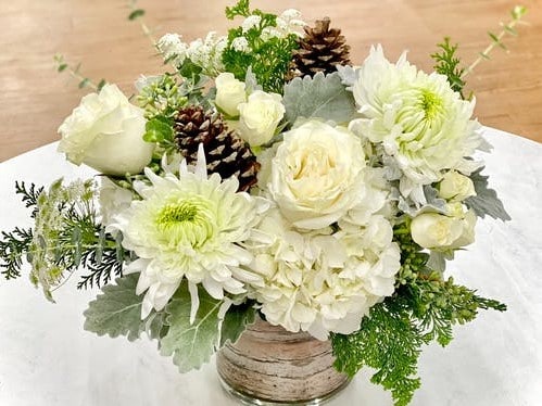 Soft and sweet natural arrangment of white flowers accented with gray dusty miller, eucalyptus and pinecones. 