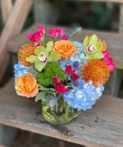 brilliantly colored arrangement features orange leucospermum pincushions, blue hydrangea, blue sea holly, coral roses and hot pink spray roses.
