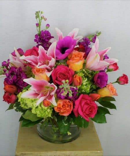 A captivating assortment of vibrant tones. This vase features fragrant lilies and other garden flowers in shades of peach, orange, purple and pink.