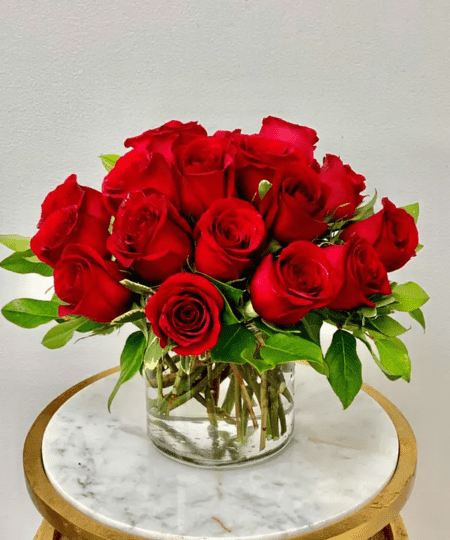 Twenty premium red roses compactly arranged in a 5" cylinder vase with lush greenery.